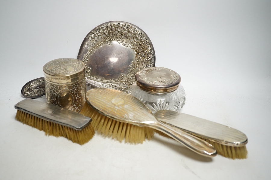 A group of Edwardian to 1920s silver dressing table items, to include three brushes, a hand mirror, a mounted glass jar, together with a South East Asian white metal jar and cover. Condition - mostly fair